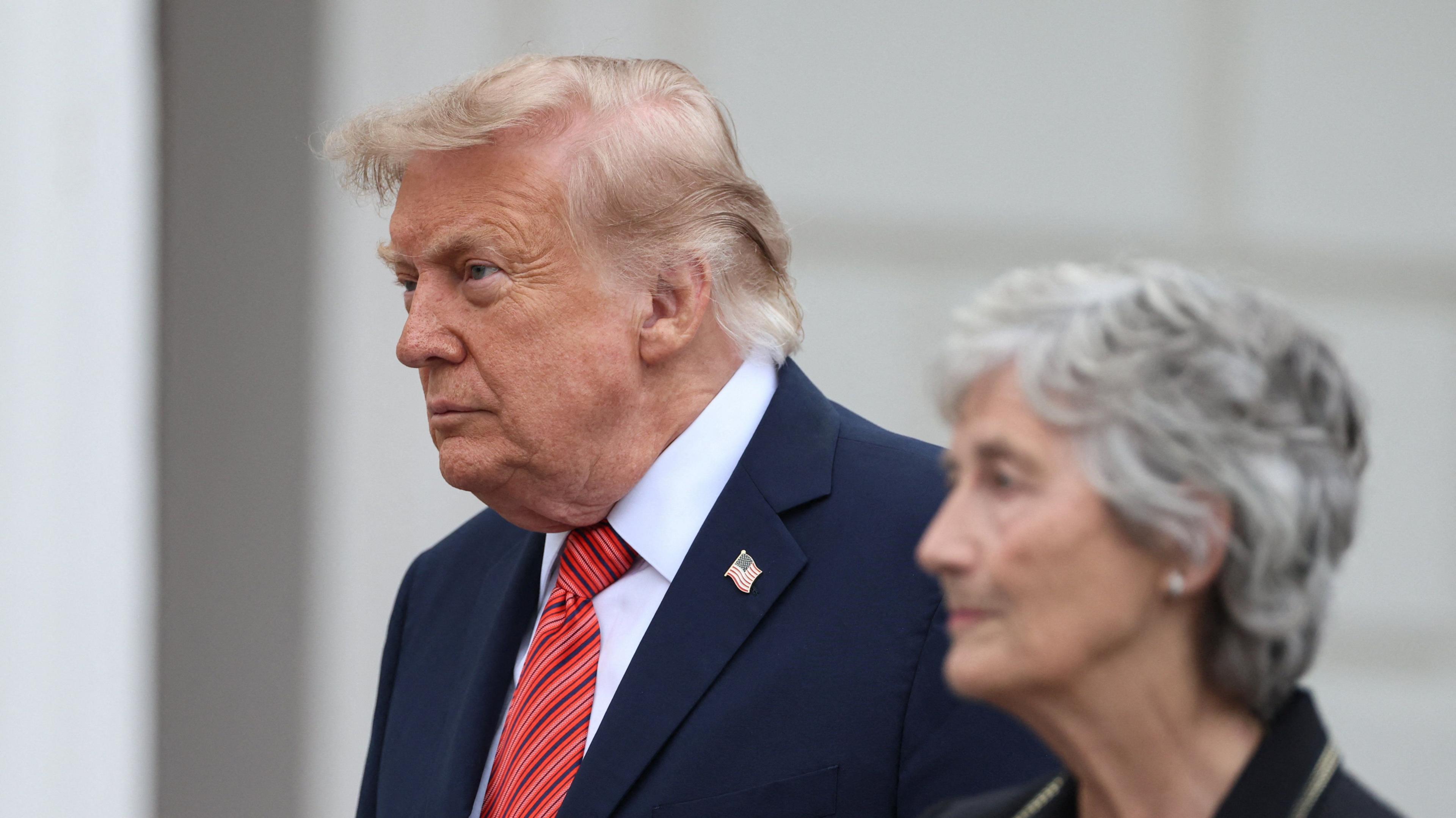 Donald Trump, light grey hair, in dark suit, red tie, is standing beside Irish President Catherine Connolly who has short grey hair and is wearing a black suit.