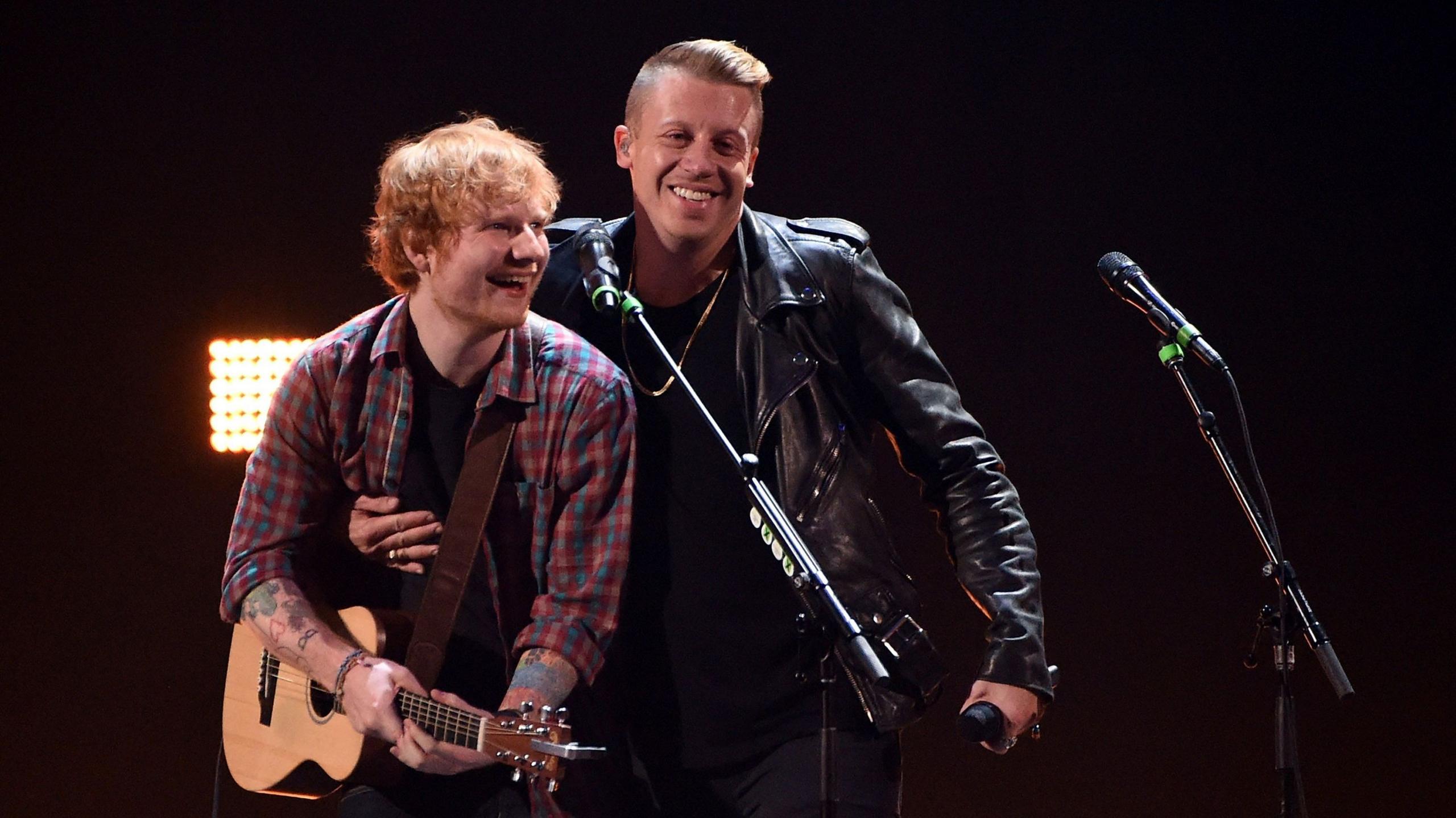 Singer/songwriter Ed Sheeran (L) and rapper Macklemore perform during the 2014 iHeartRadio Music Festival at the MGM Grand Garden Arena on September 20, 2014 in Las Vegas, Nevada. Sheeran is wearing a checked shirt and holding a guitar. Macklemore is wearing a black jacket.