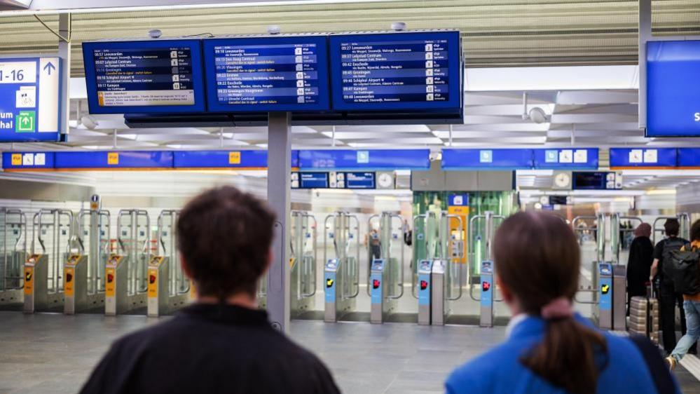 Two people are seen from behind looking up at an information board at Zwolle station in Zwolle, Netherlands, where trains are facing significant disuption