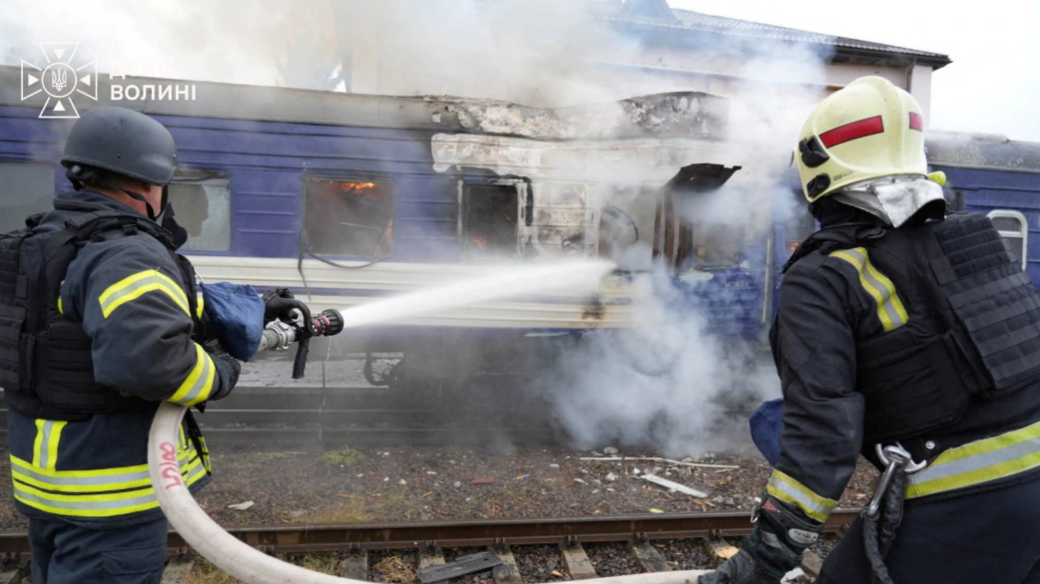 Two firefighters battle a blaze on a blue and white train after a Russian drone hit it in Ukraine