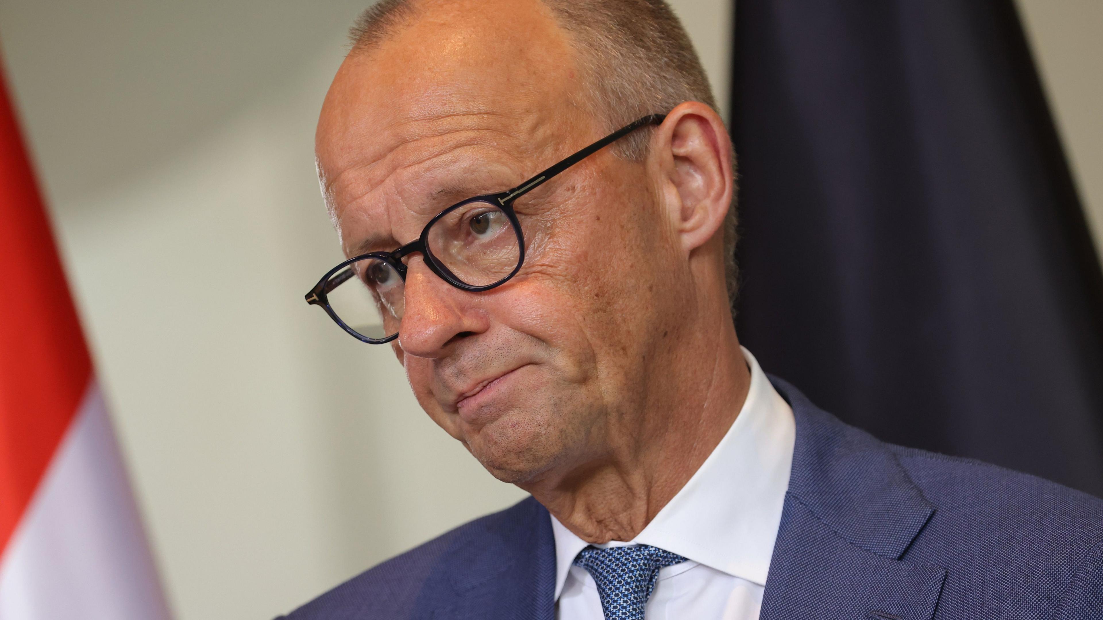 German Chancellor Friedrich Merz appears at a news conference wearing a blue suit and tie, white shirt and glasses.