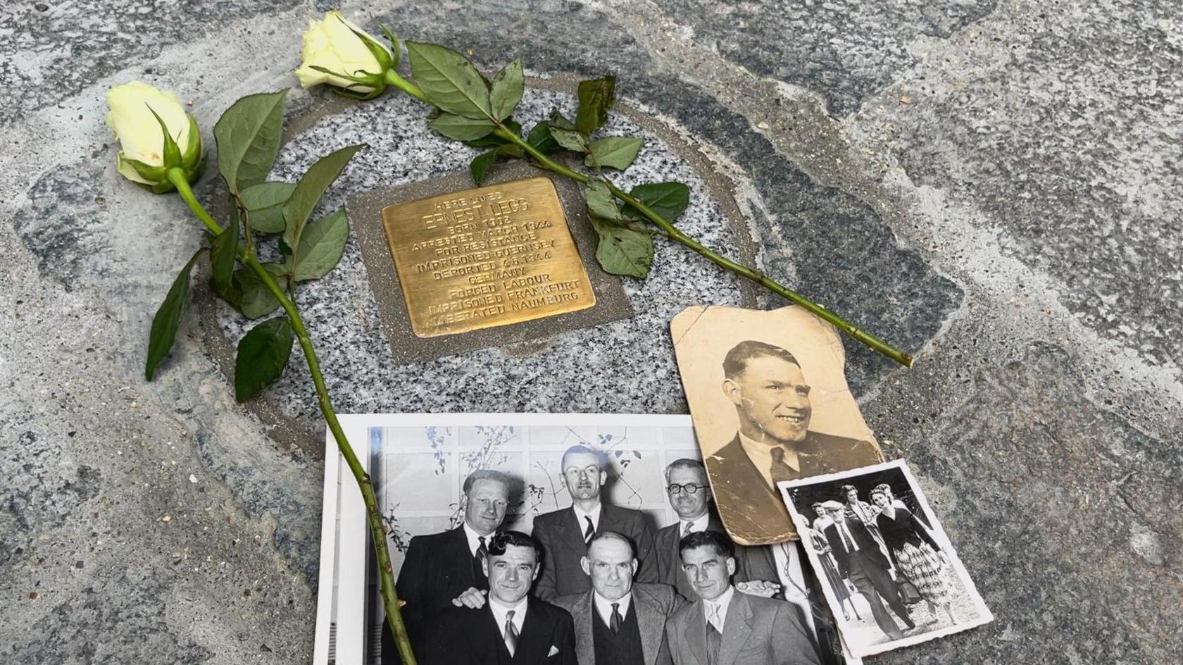 A commemorative brass plaque and grey stone. Aged photos of Legg and others, along with two white roses lay atop the stone.