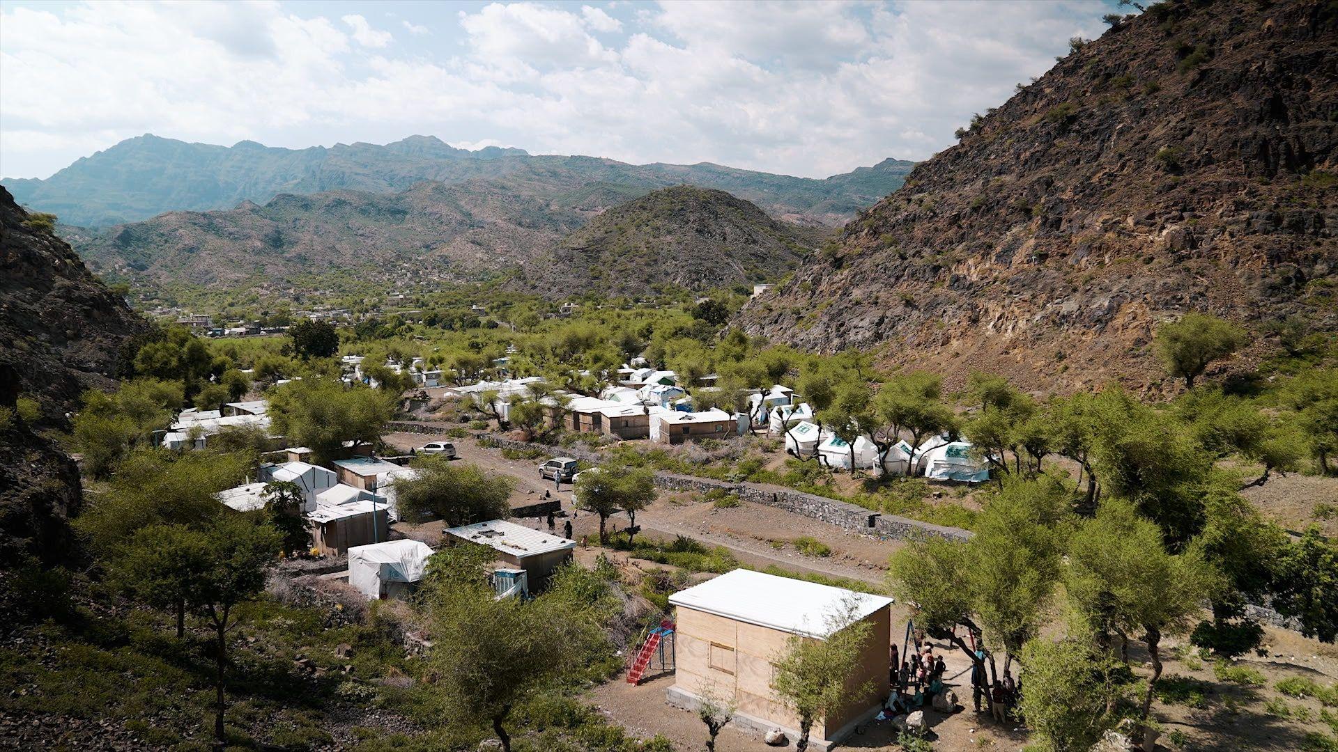 At the the al-Monig displacement camp, tents stand among trees in a valley bottom, surrounded by stony hills