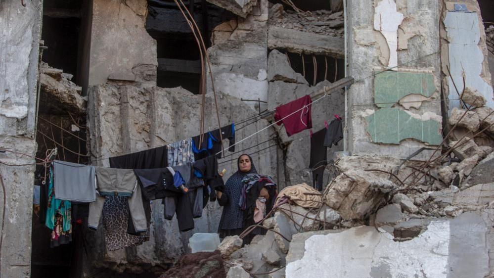 A displaced Palestinian woman collects laundry hanging inside a destroyed building in Gaza City. Photo: 21 September 2026.