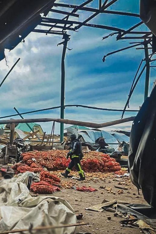 Piles of onions strewn on the ground in a farm structure that's been hit by a Russian strike. An emergency worker is inspecting the scene.