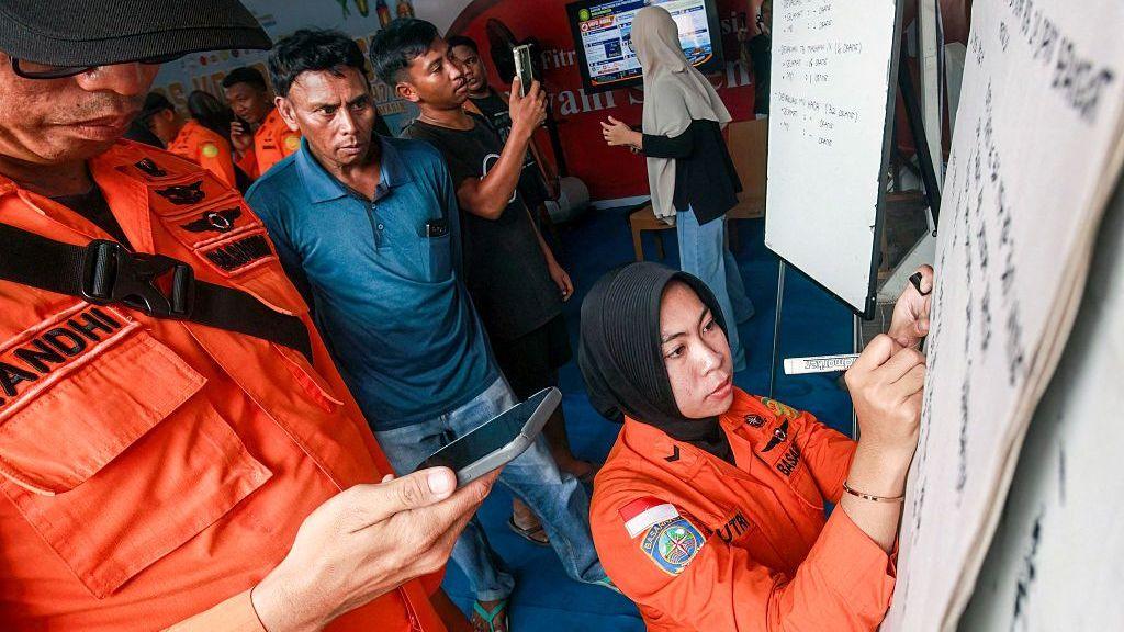 Relatives of affected passengers look on as a National Search and Rescue Agency (Basarnas) officer writes updates on a whiteboard amid ongoing rescue operations on the stricken Virgo Transport 8 ferry, at Trisakti Bandarmasih Port in Banjarmasin, South Kalimantan, on September 13, 2026.