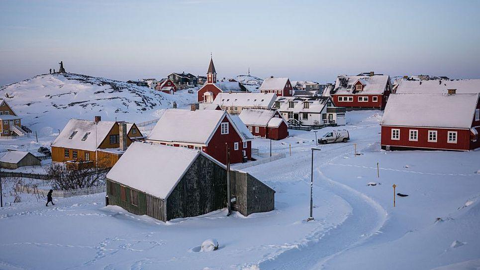 Snow covers houses in Nuuk, Greenland. Some houses are red, with a church in the background