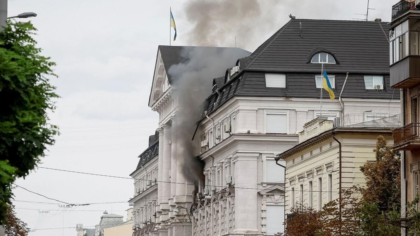 Black smoke pours from two windows in a large government building with Ukrainian flags on the facades.