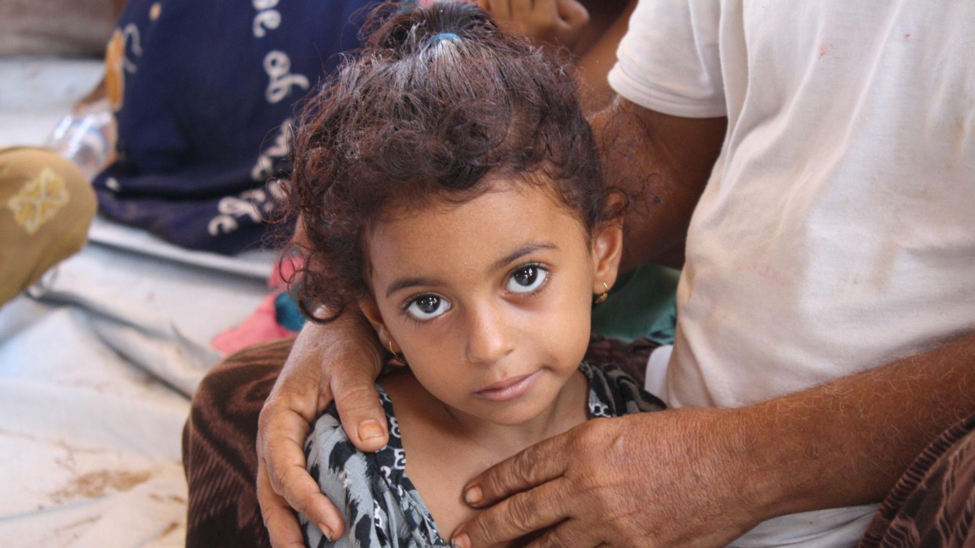 A refugee girl held by her father looks up at the camera