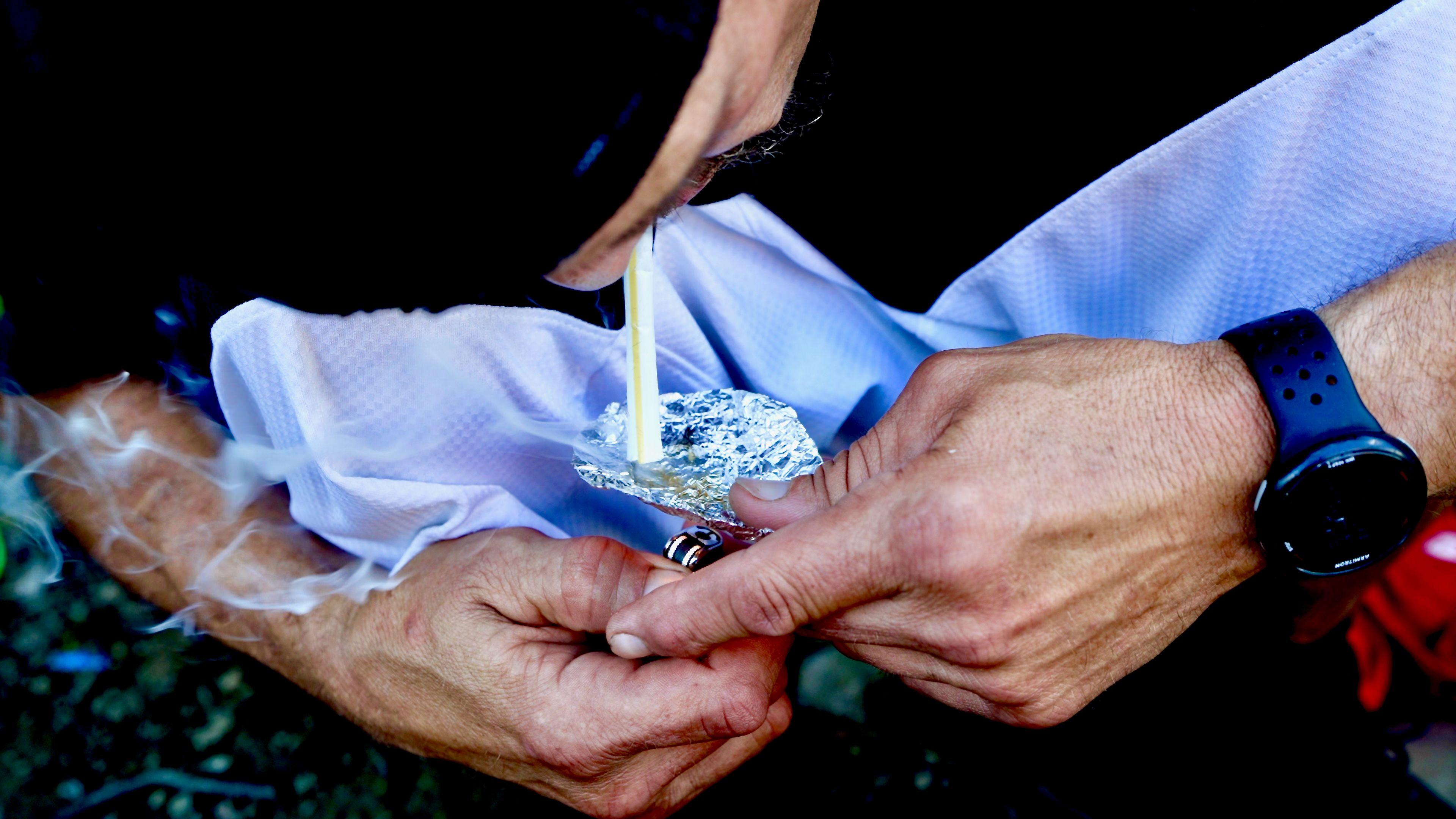 Close-up shot of Mike using a cigarette lighter to light up a few grains of fentanyl placed on some silver foil