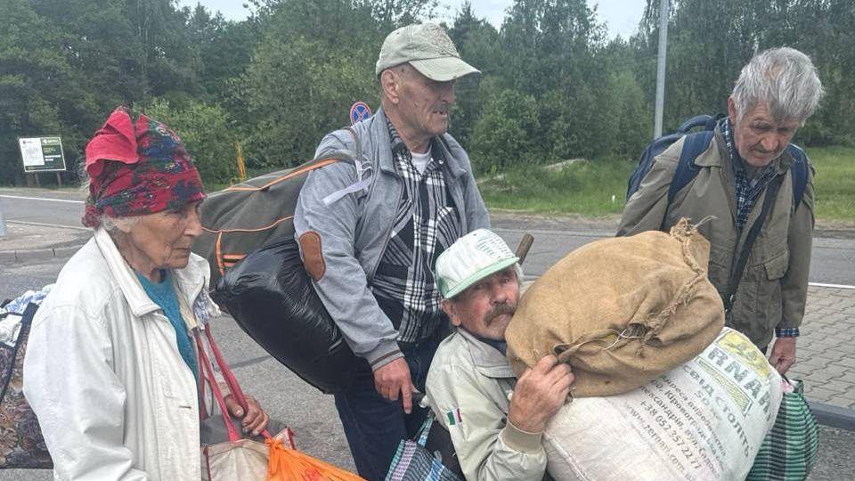 Four elderly people wearing coats and carrying belongings