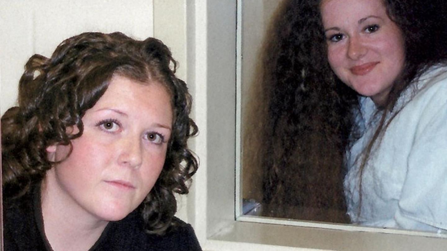 Helen roberts pictured at the forefront of the photograph, with Christ Pike behind her. The pair are separated by a glass window and both have brown curly hair and brown eyes.