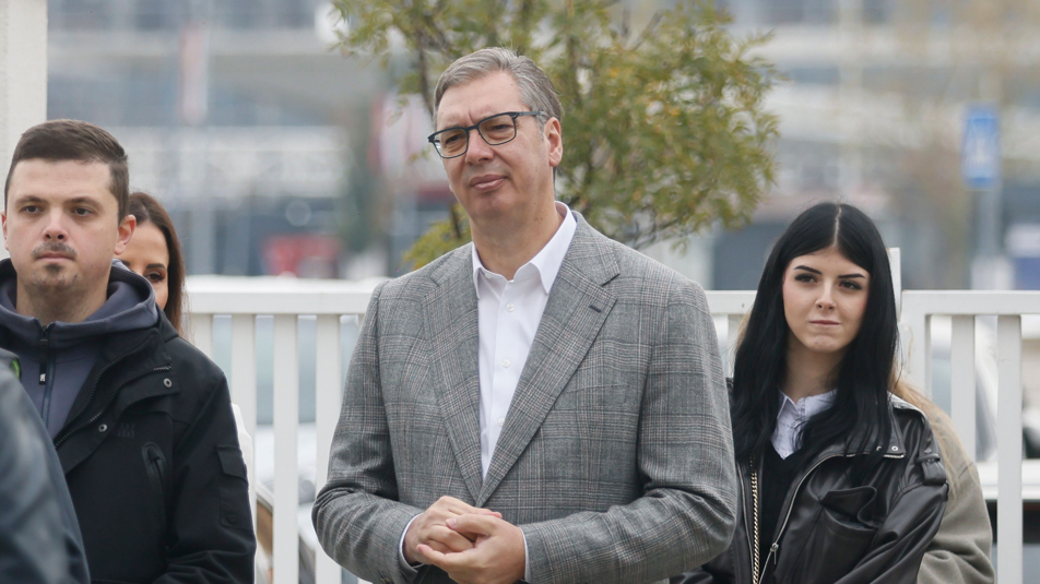 Aleksandar Vucic in a grey suit and white shirts waits in a polling station queue