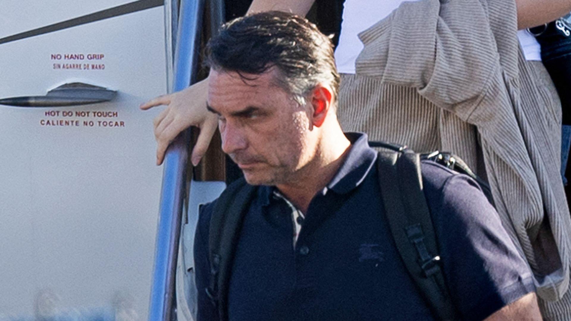 Bolsonaro in a dark shirt carrying a backpack as he leaves a plane