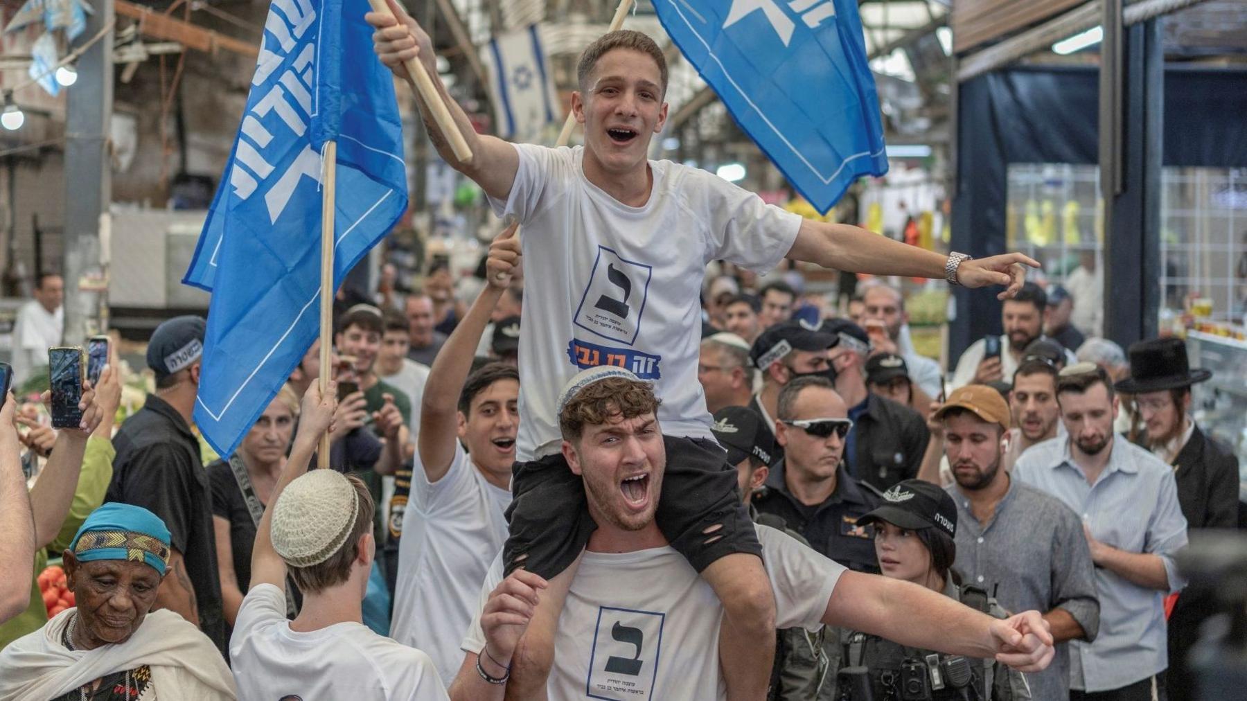 Supporters of Israel's far-right National Security Minister Itamar Ben-Gvir wave blue flags of his Jewish Power party as he tours Ramle market, Israel (14 October 2026)