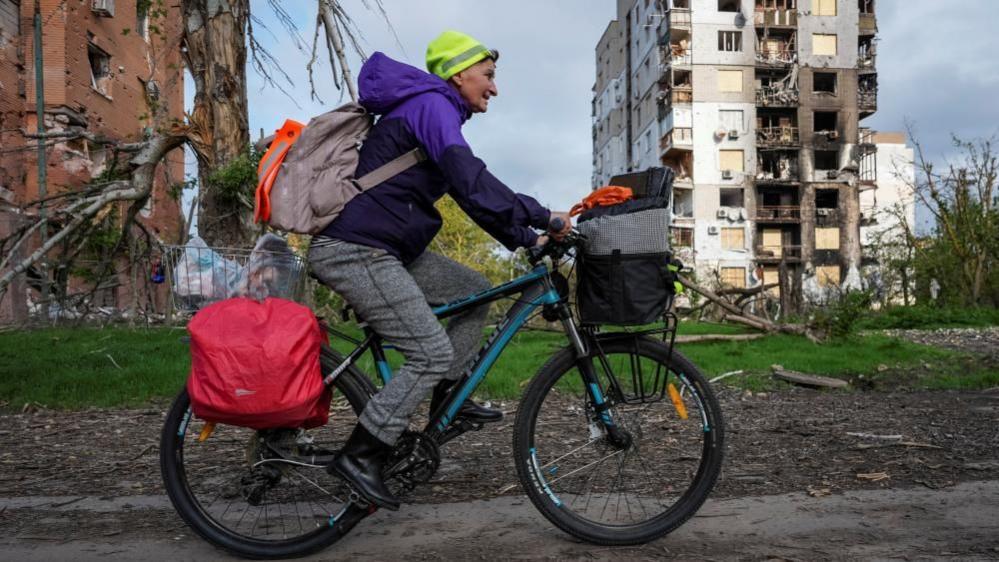 A woman cycles among destroyed buildings