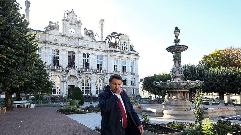 Limoges' mayor Guillaume Guérin walks in front of the partially burnt city hall a day after riot and looting following nationwide protests against the "high cost of living"
