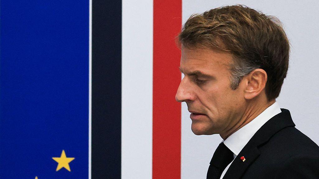 Close up of French President Emmanuel Macron taken from the side. He has short brown hair, and is wearing a white shirt, black jacket and tie.