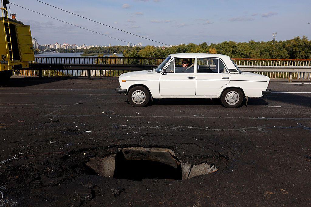 A white car drives next to a hole in the concrete road on Kyiv's Pivnichnyi Bridge, which was hit by a Russian drone.