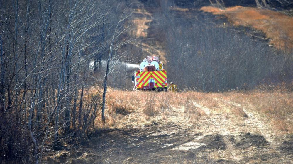 A fire truck sprays water on dry grass and trees near Wainwright