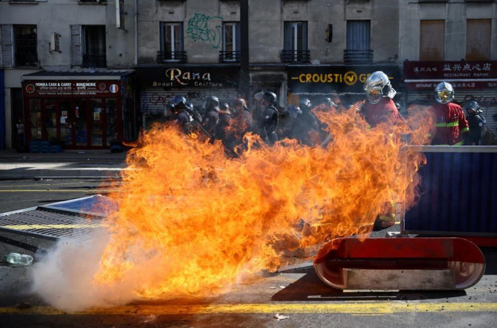 A huge plume of flames jumps across the street scene as two firefighters use extinguishers to try and bring it under control