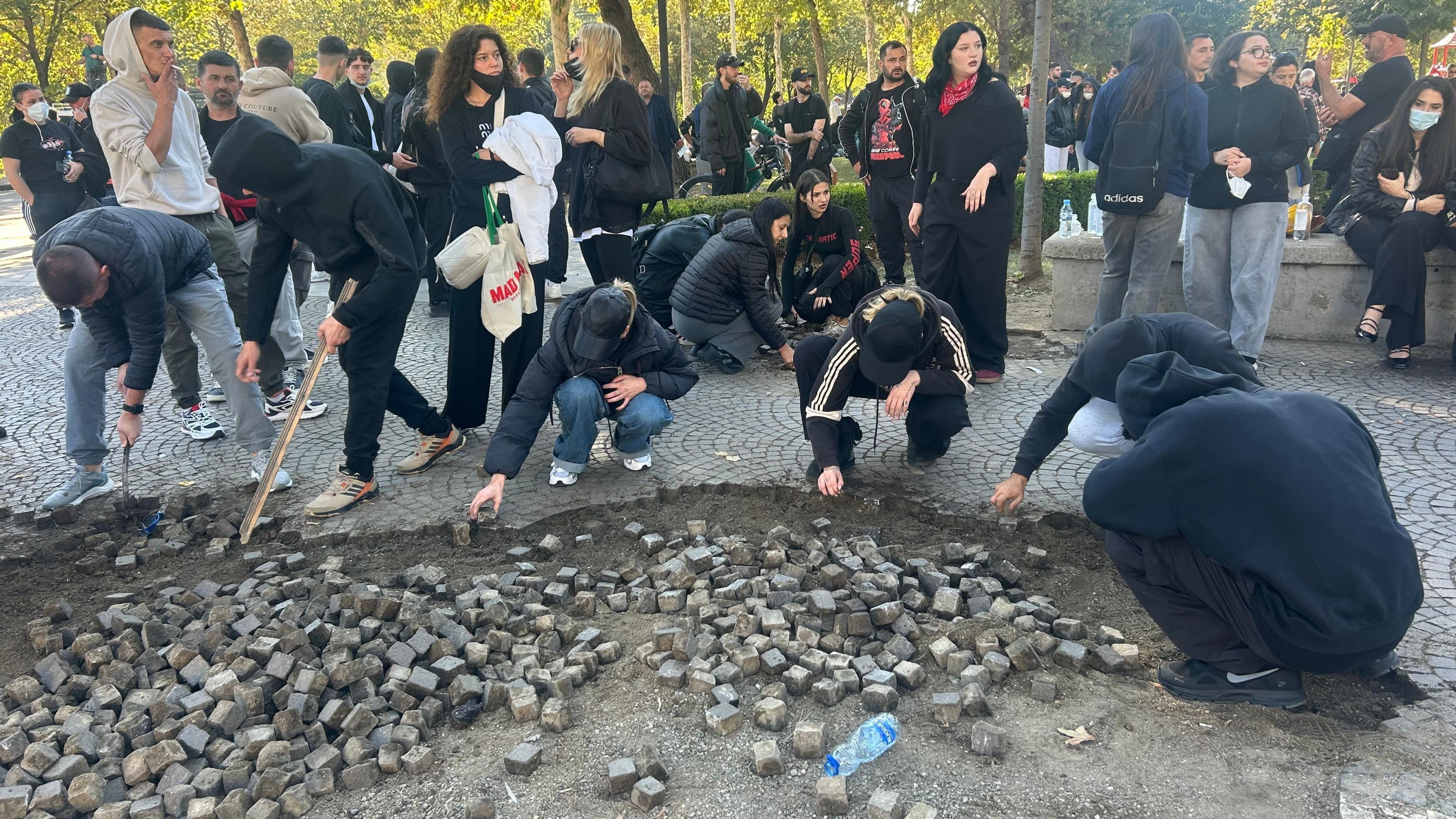 Crouching people use hands and bits of wood to loosen cobblestones.