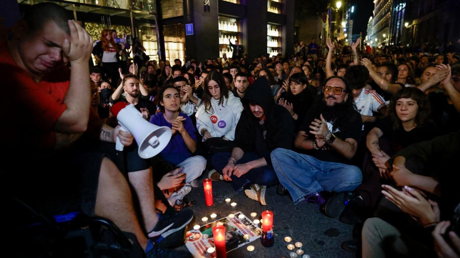People gather in one of Madrid's main squares, Puerta del Sol, following the death of Maricarmen Abascal. One man can be seen carrying a megaphone as he appears emotional, while others sit crossed legged. Candles have been lit in memory of Maricarmen.