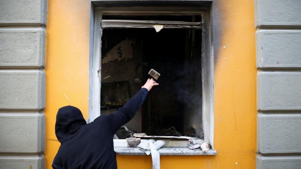 A man throws a brick into the broken window of Albania's education ministry