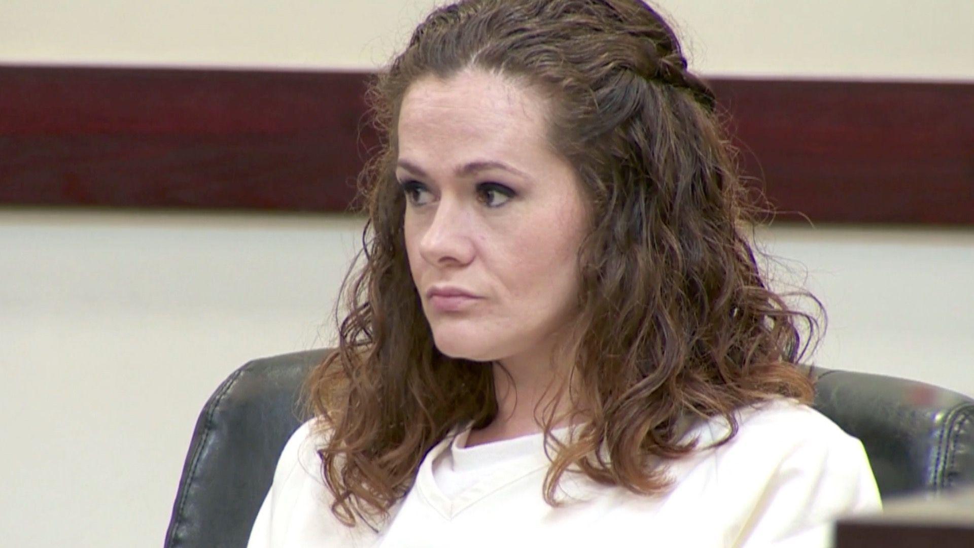 A woman in a white prison uniform sits in court.