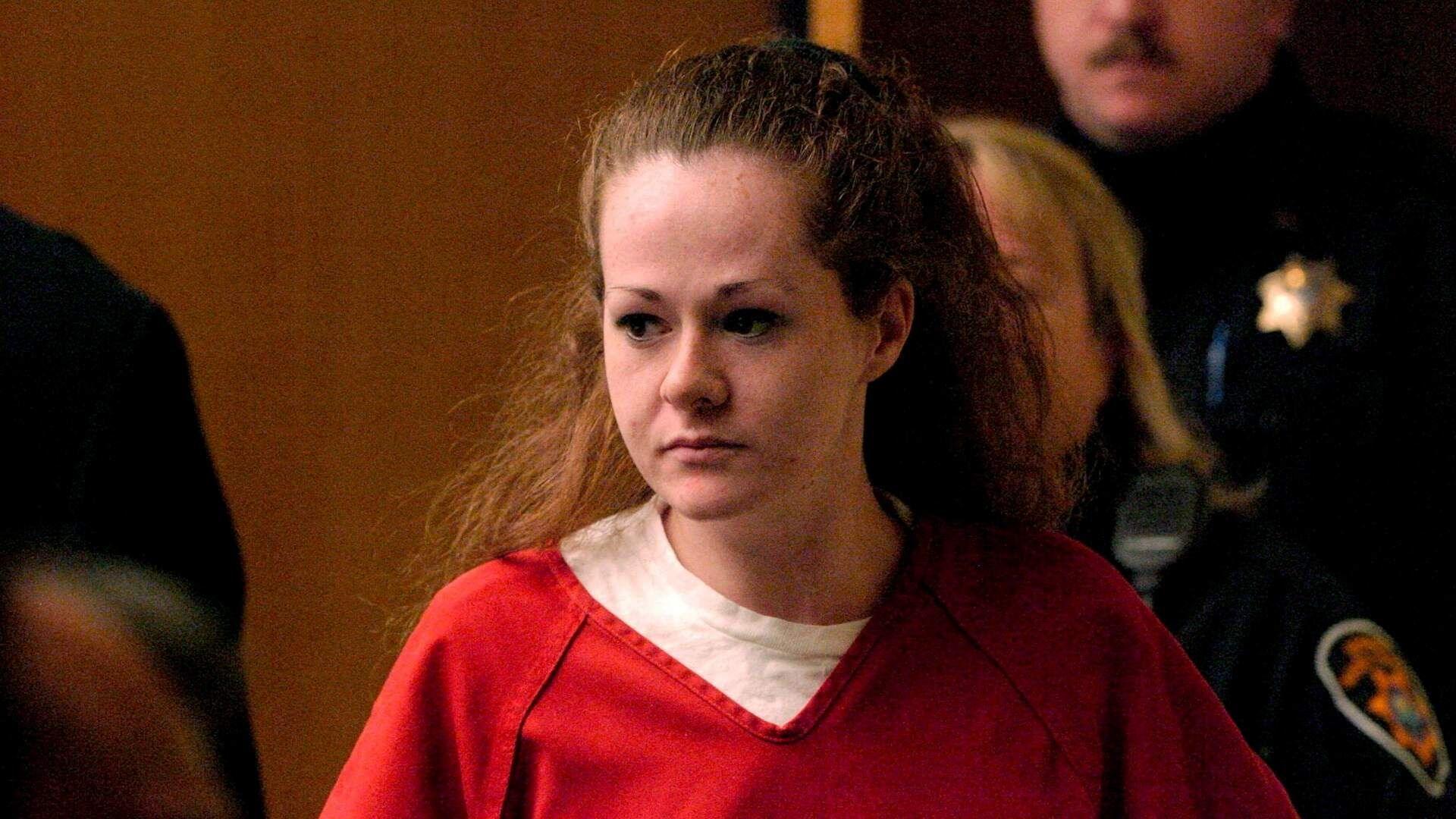 A woman with red hair wears a red jumpsuit